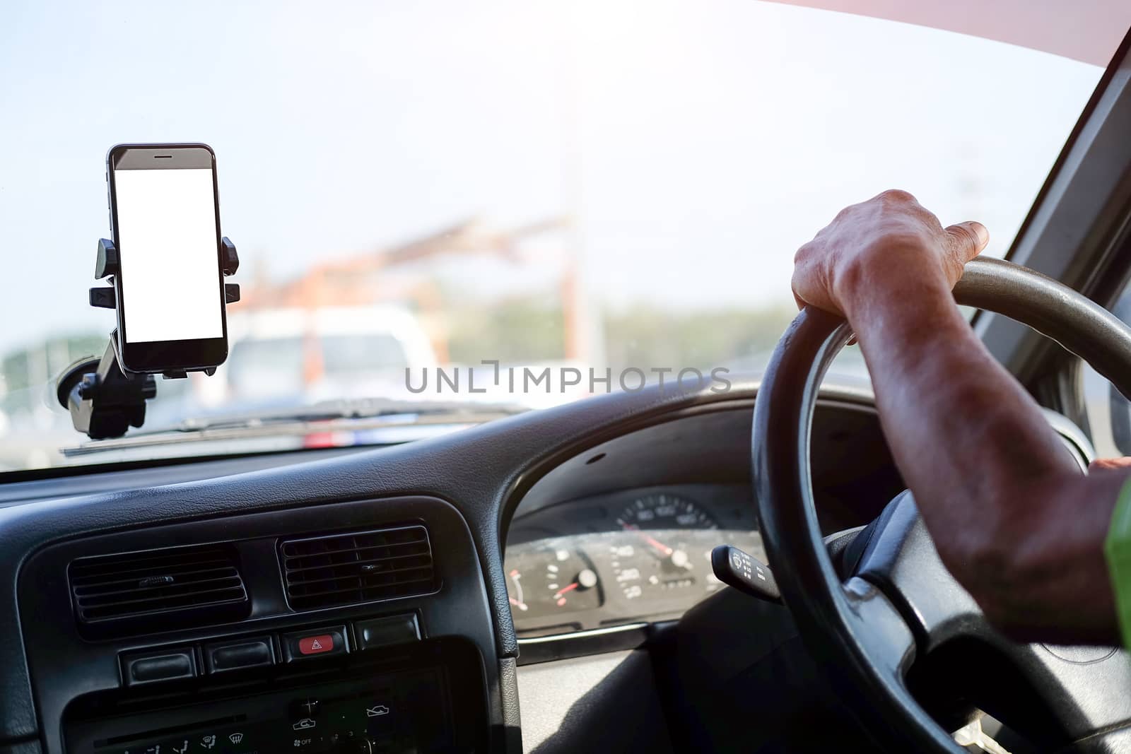 Cropped shot view The driver uses the phone while driving. Modern smart phone with round edges. Isolated screen for mockup. Car navigation display in background. 