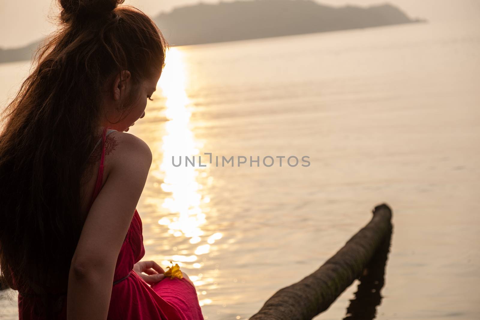 Woman sits on palm tree admiring the sunset on Chapora, GOA, India