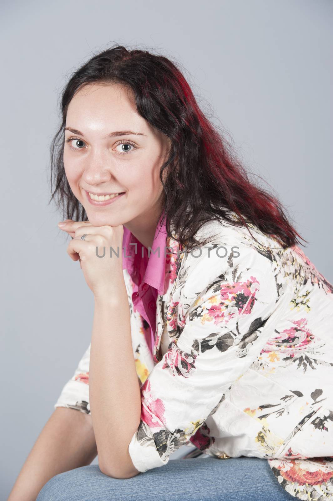 Beautiful young happy brunette girl posing in studio wearing pink blouse isolated on grey background