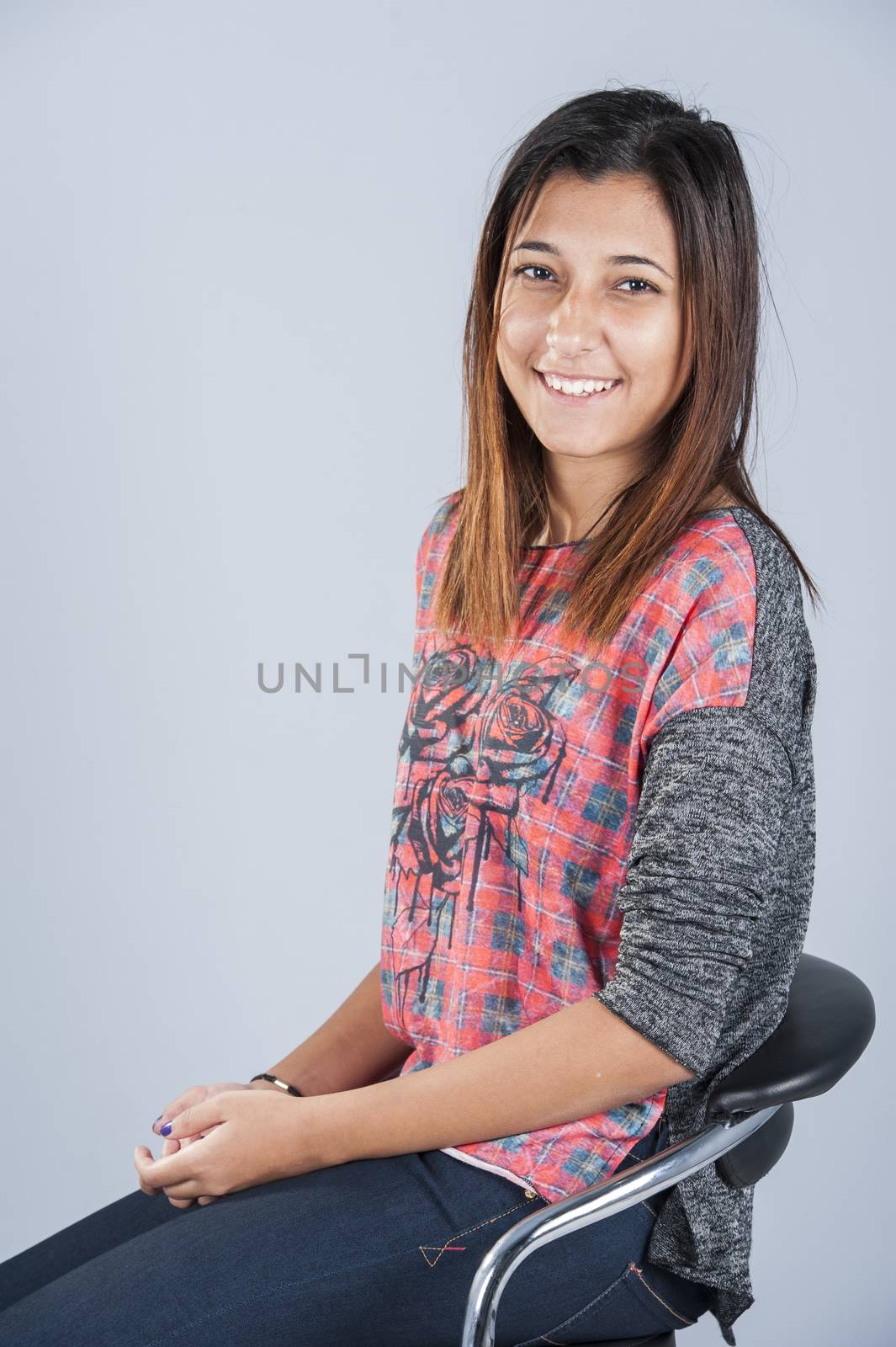 Beautiful young happy brunette girl posing in studio whilst sitting in chair