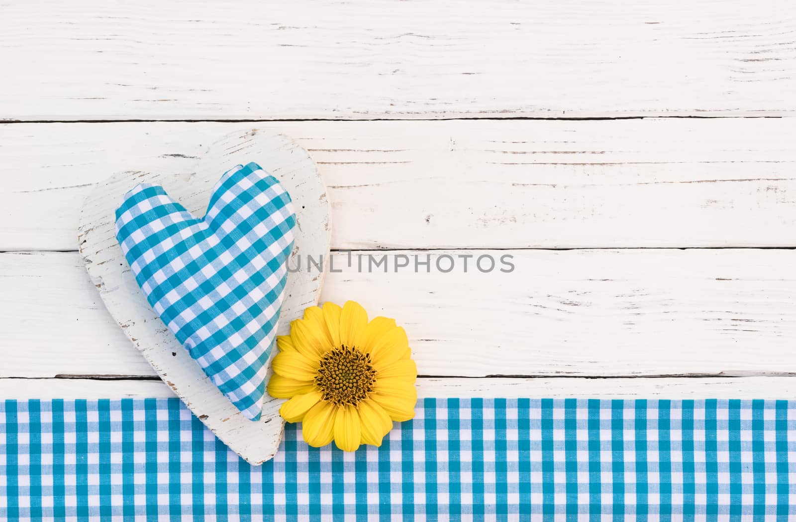 Blue fabric heart with yellow blossom on white wood background with copy space