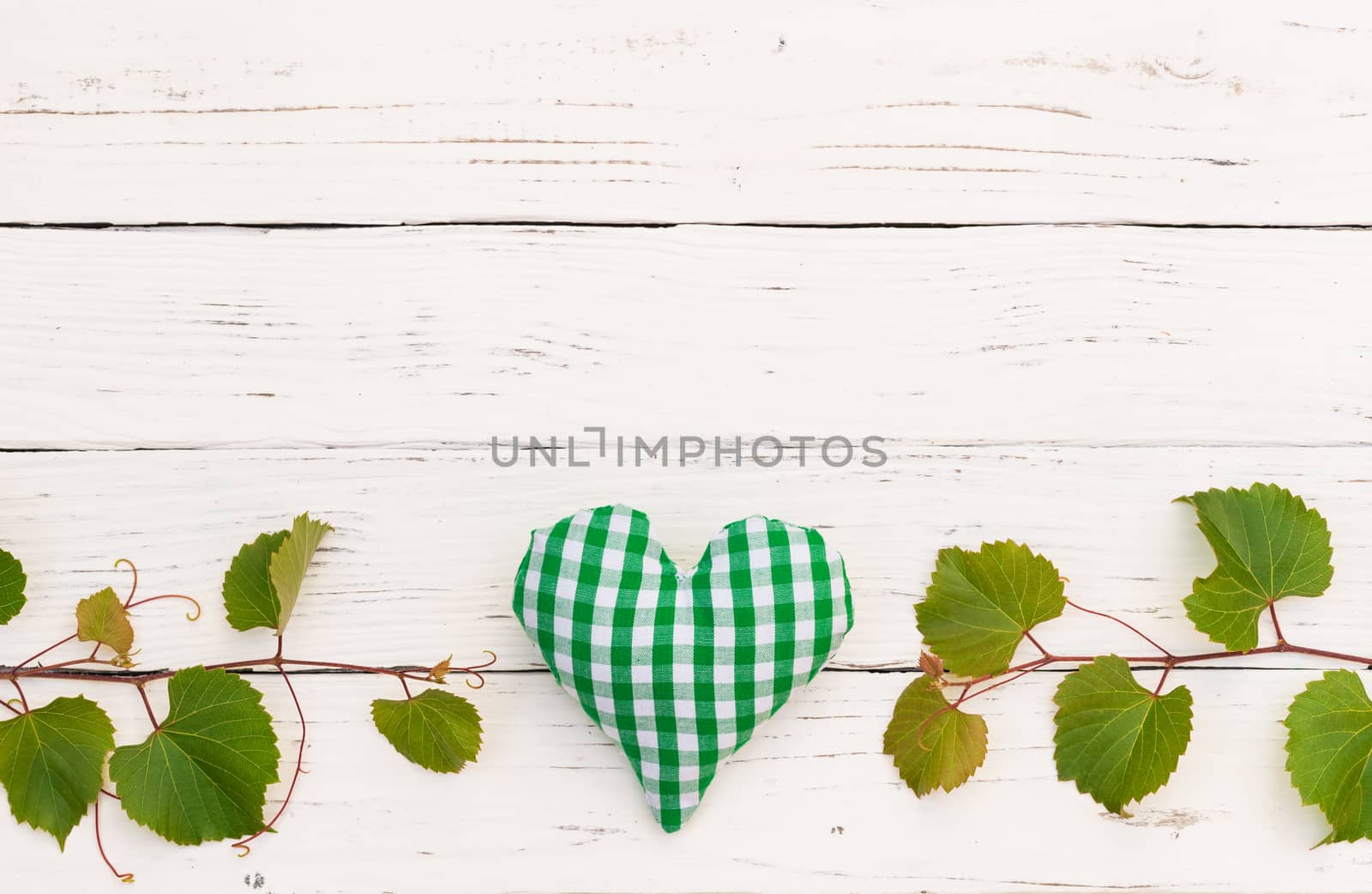White wooden background with green vine leaves border and heart for wine celebration, event or winetasting invitation