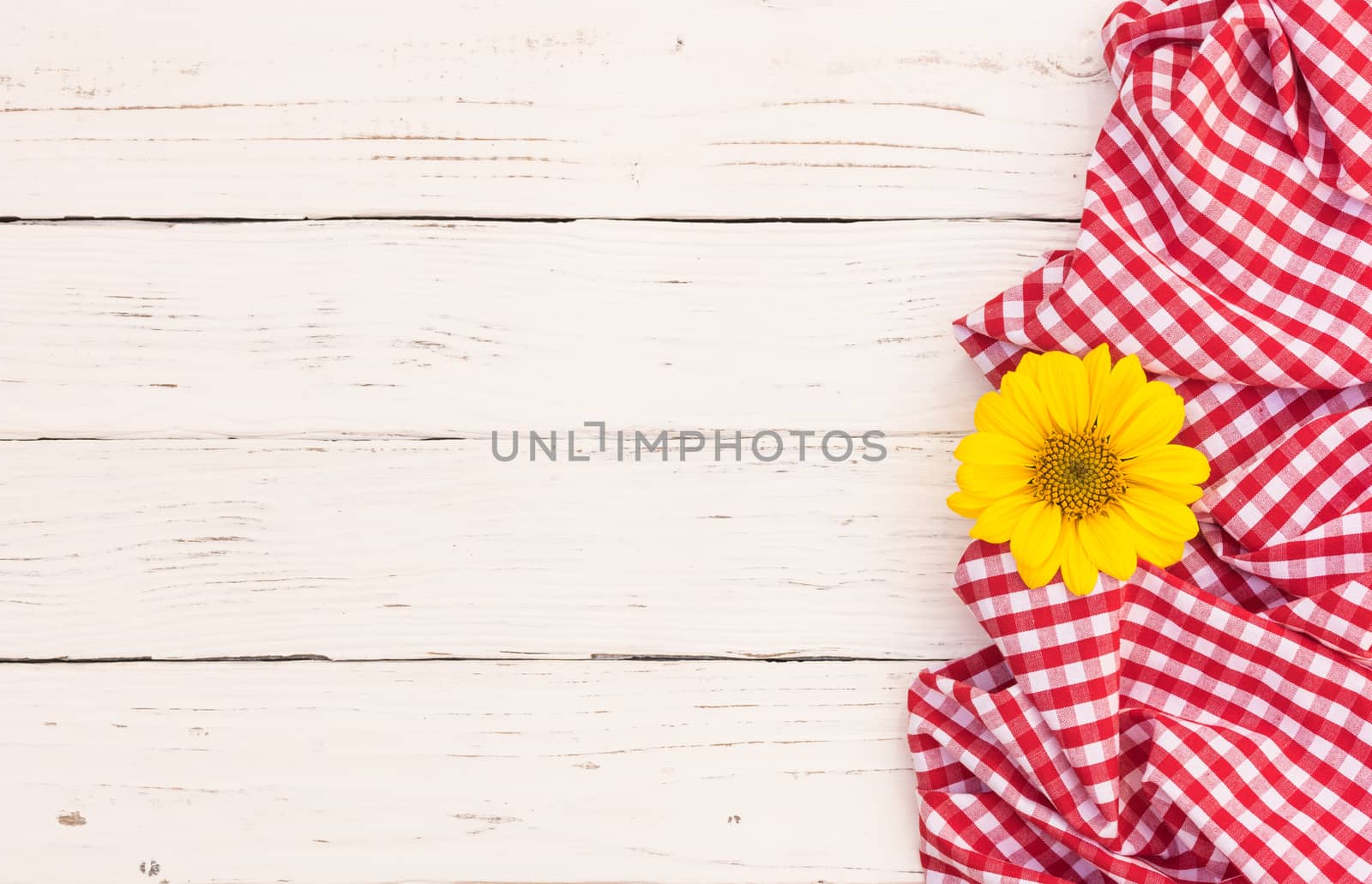 White wood table with red tablecloth and yellow blossom with copy space