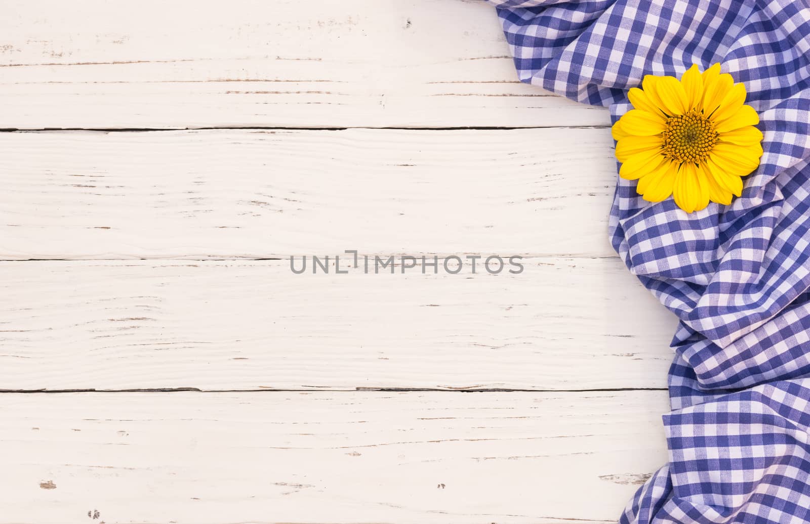 Blue tablecloth and yellow flower on white wooden table with copy space