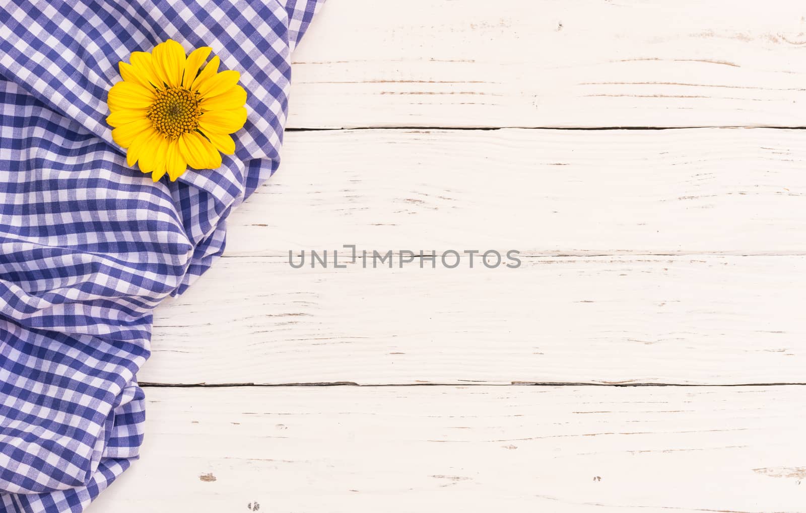 Blue checked tablecloth and yellow flower on white wooden table with copy space