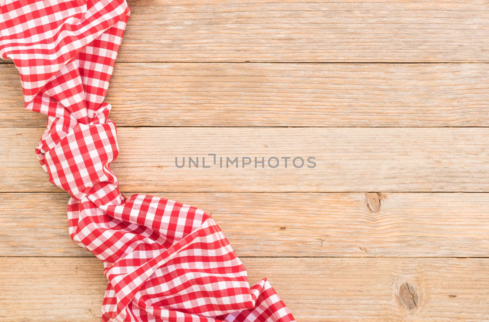 Knotted red checked tablecloth on wooden table background, top view