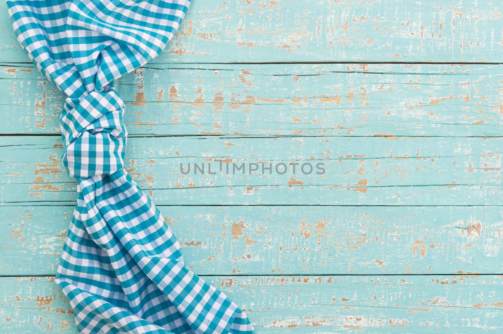 Knotted blue checked tablecloth on rustic wooden table background, top view