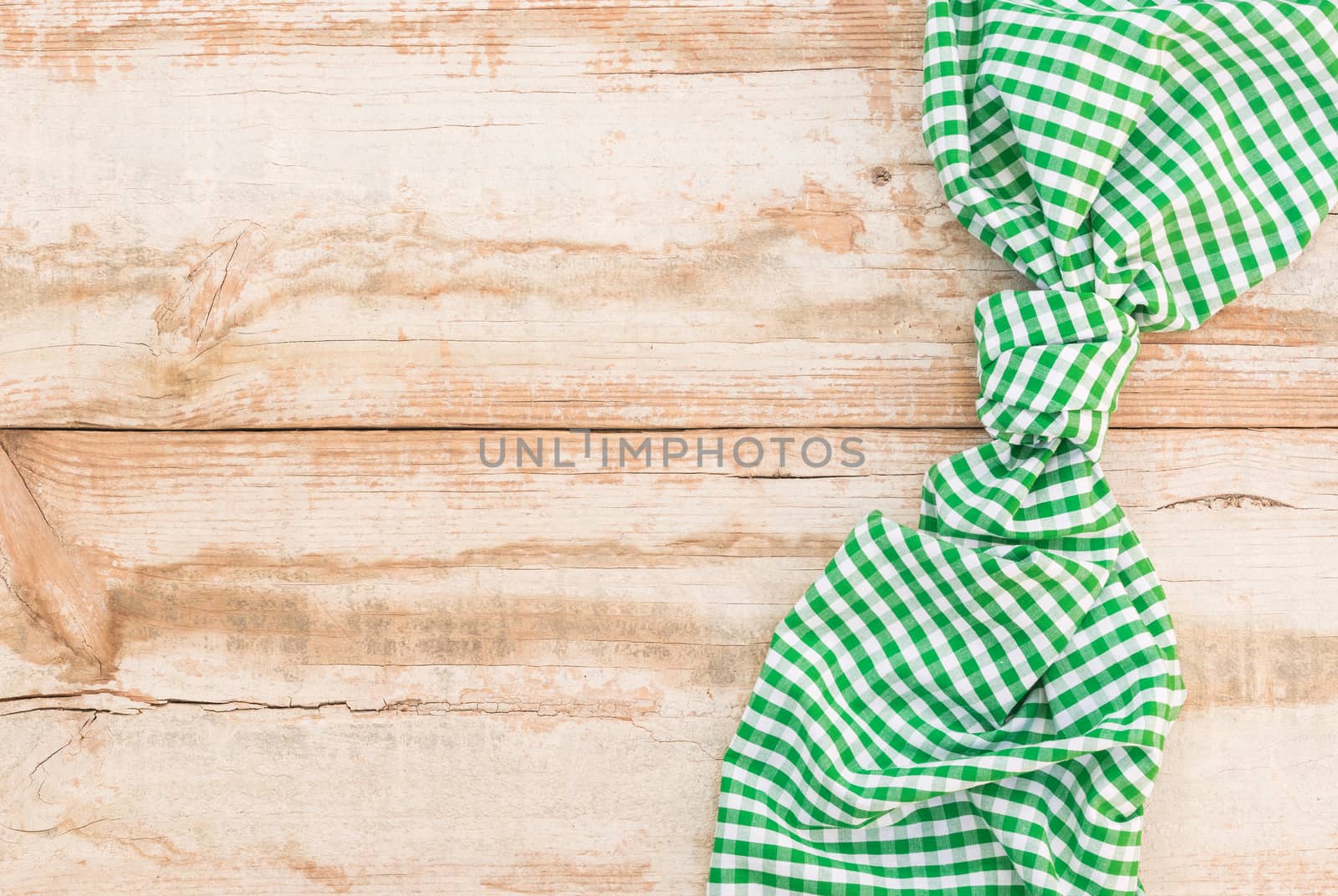 Knotted green checked tablecloth on rustic wooden table background, top view