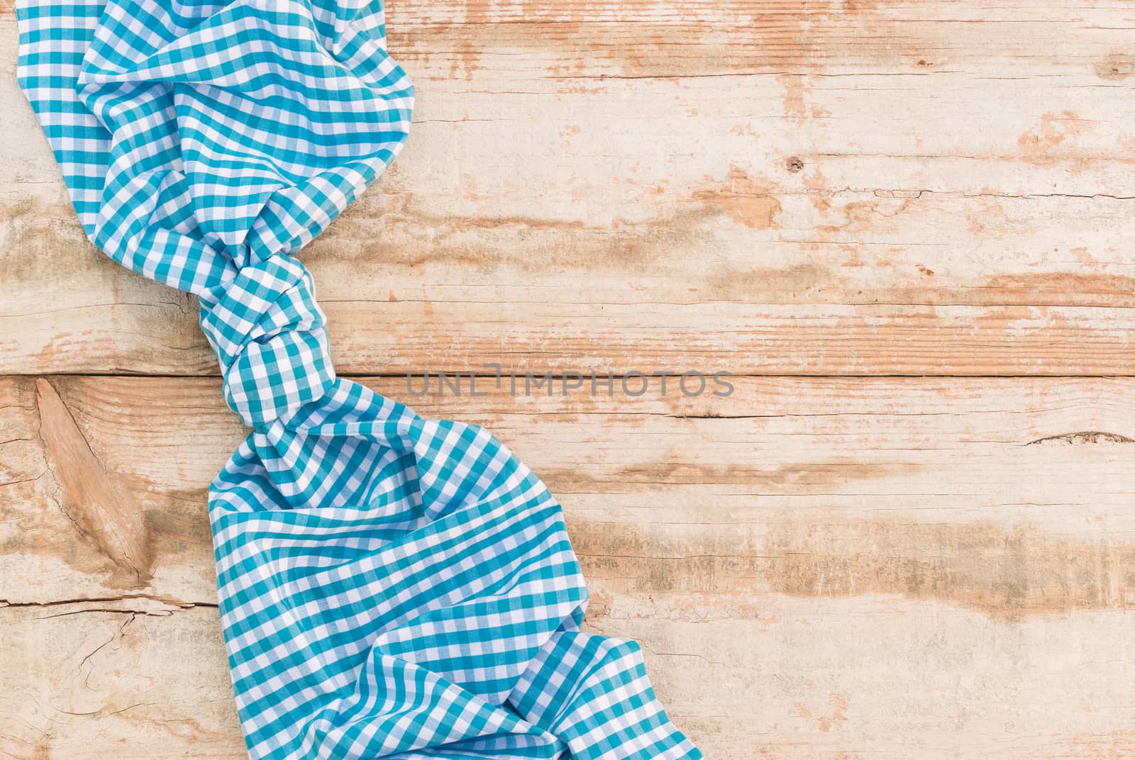 Knotted blue checked tablecloth on rustic wooden table background, top view