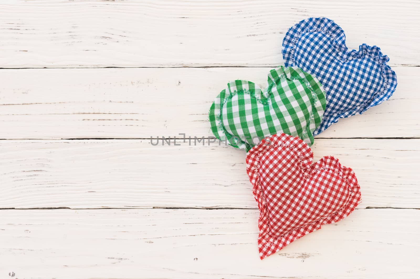 Three rustic fabric hearts on white wood background with copy space