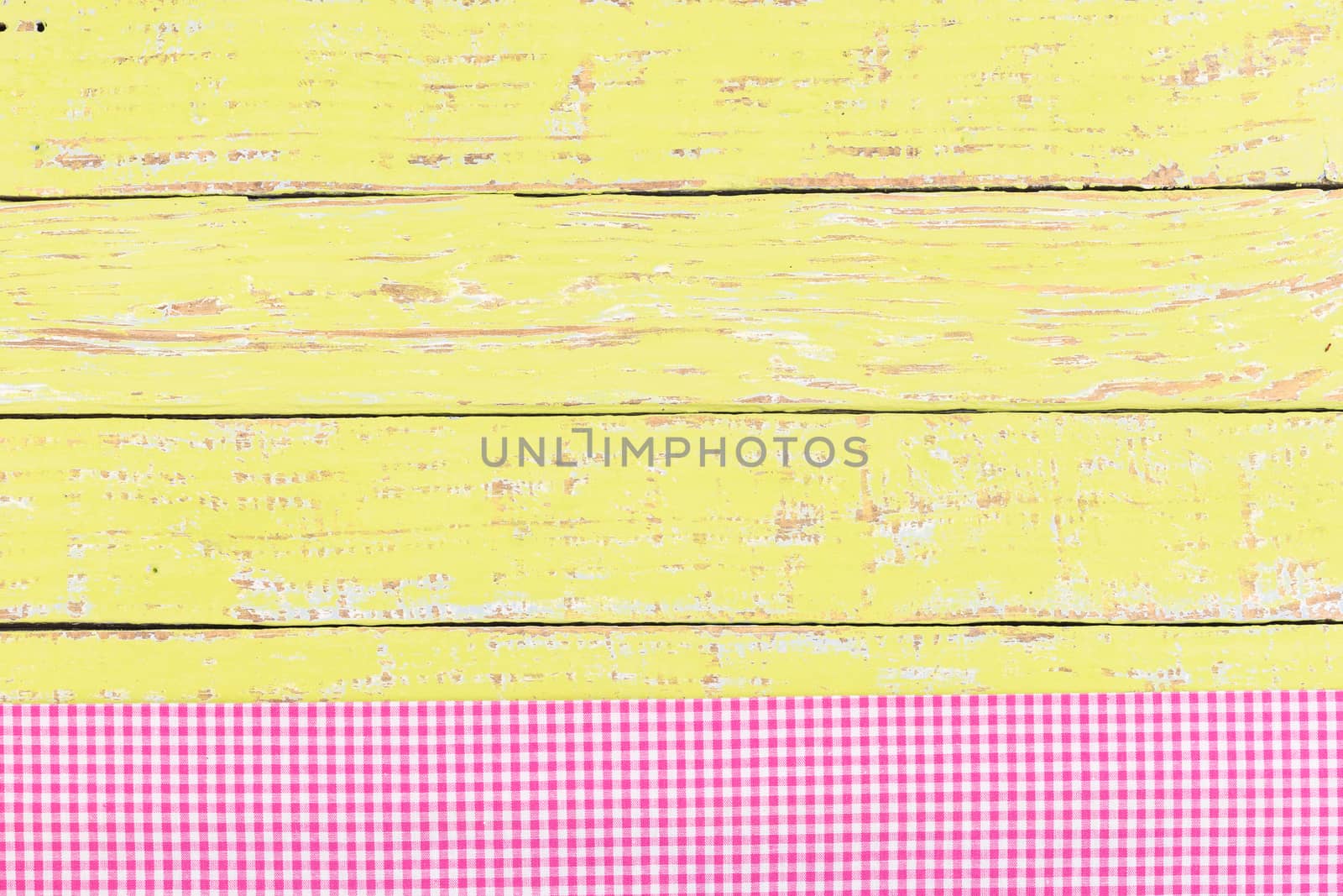 Yellow wooden table surface with pink checkered cloth, top view