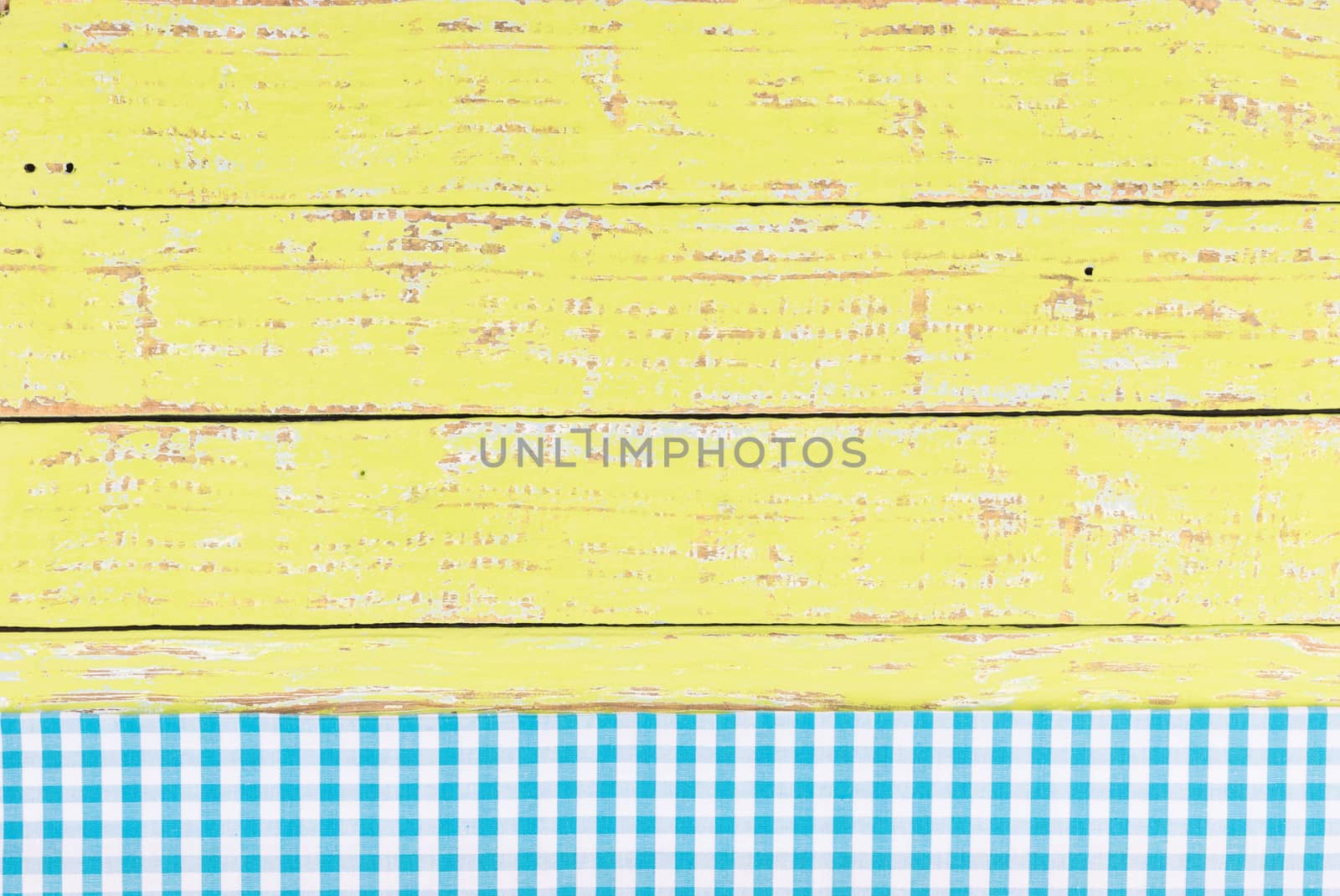 Rustic yellow wooden table surface with blue checkered cloth, top view