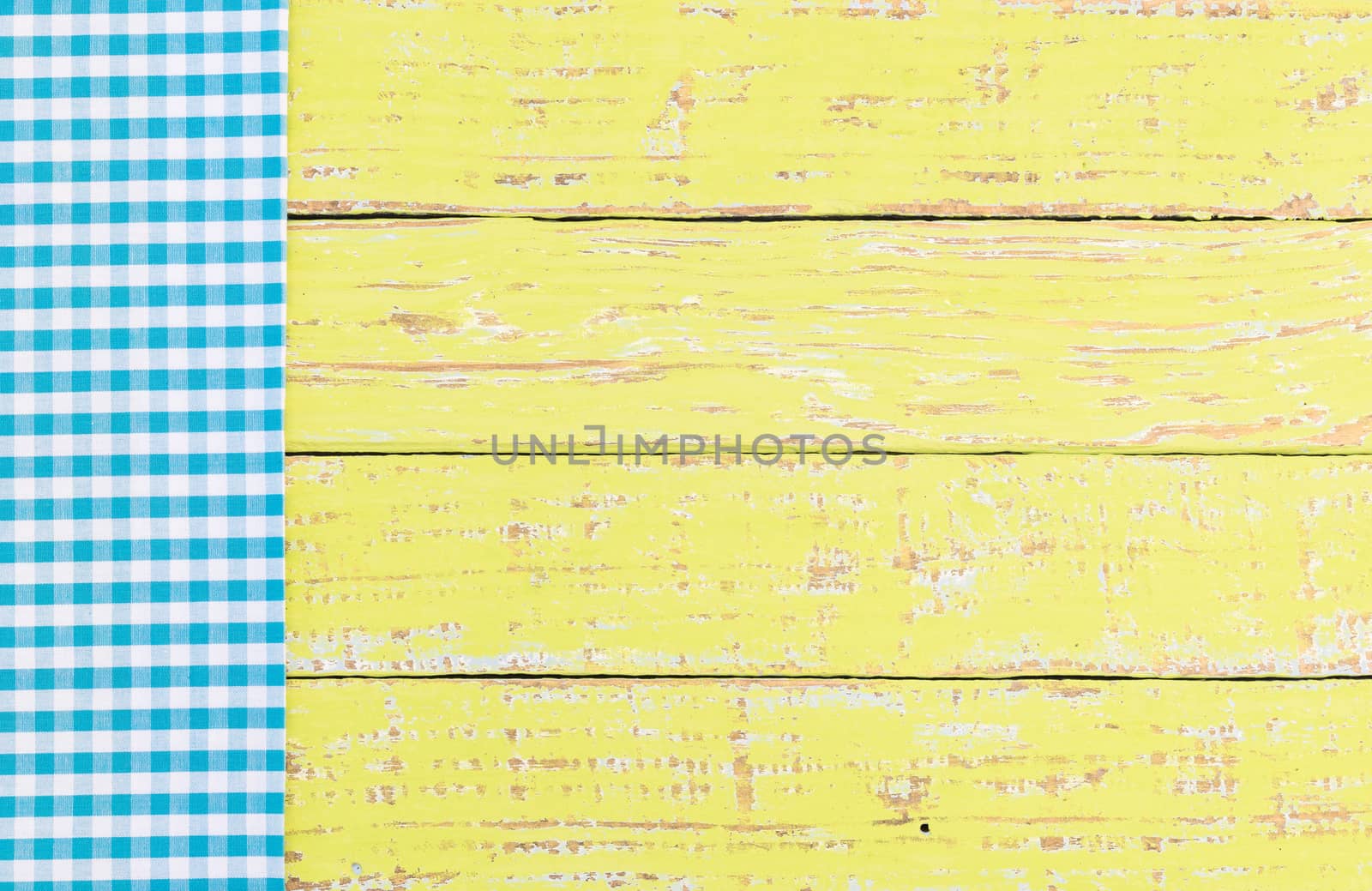Blue checked tablecloth on rustic colored wooden table background, top view