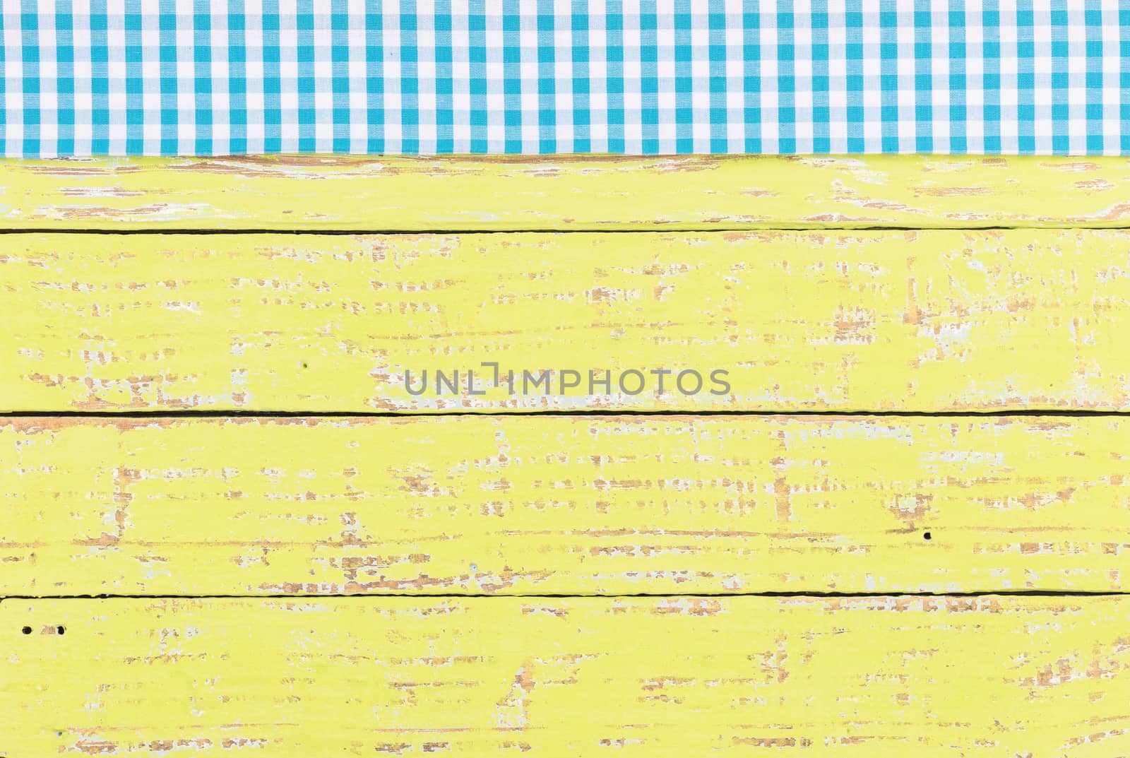 Rustic yellow wooden table surface with blue checkered cloth, top view