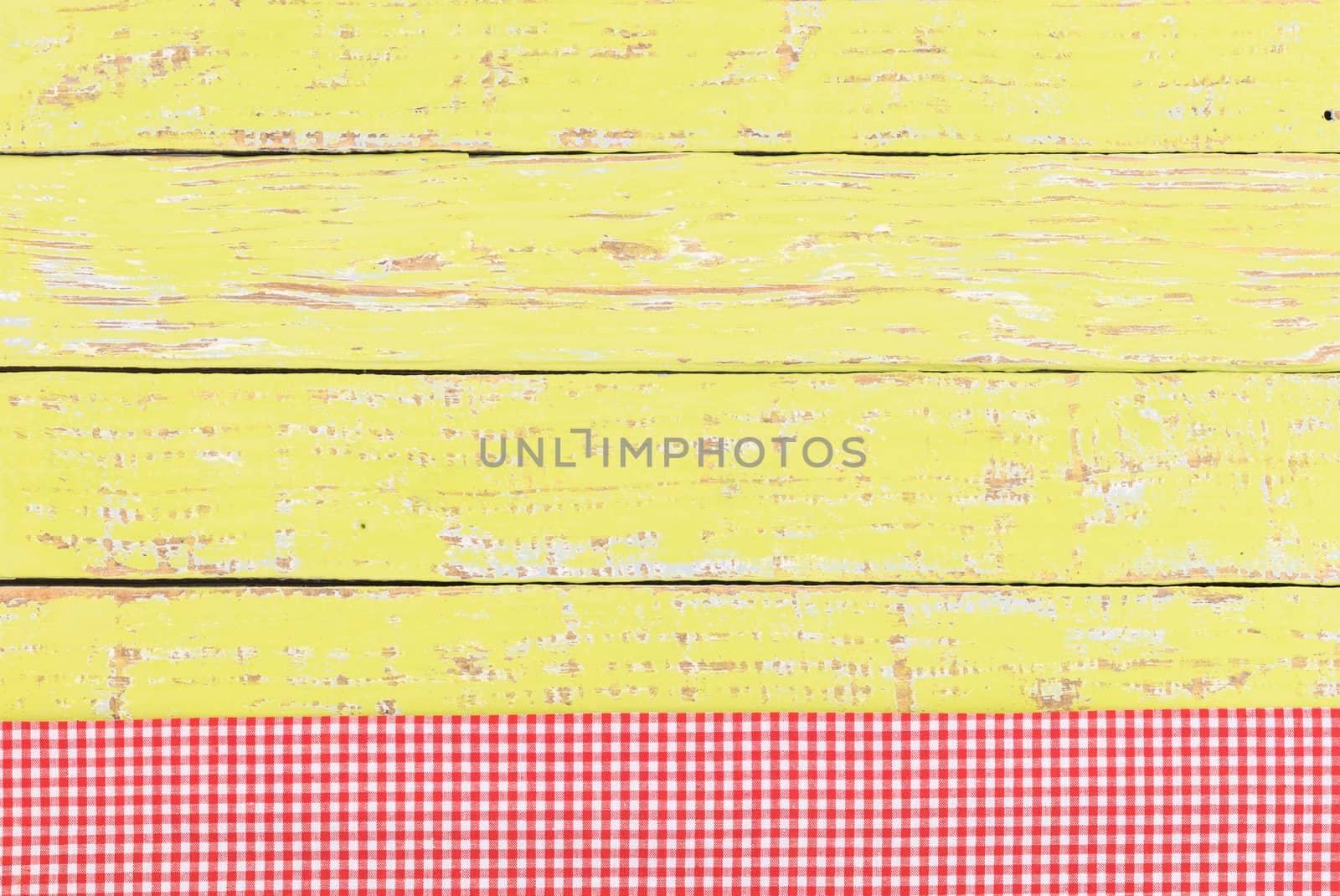 Rustic yellow wooden table surface with red checkered cloth, top view