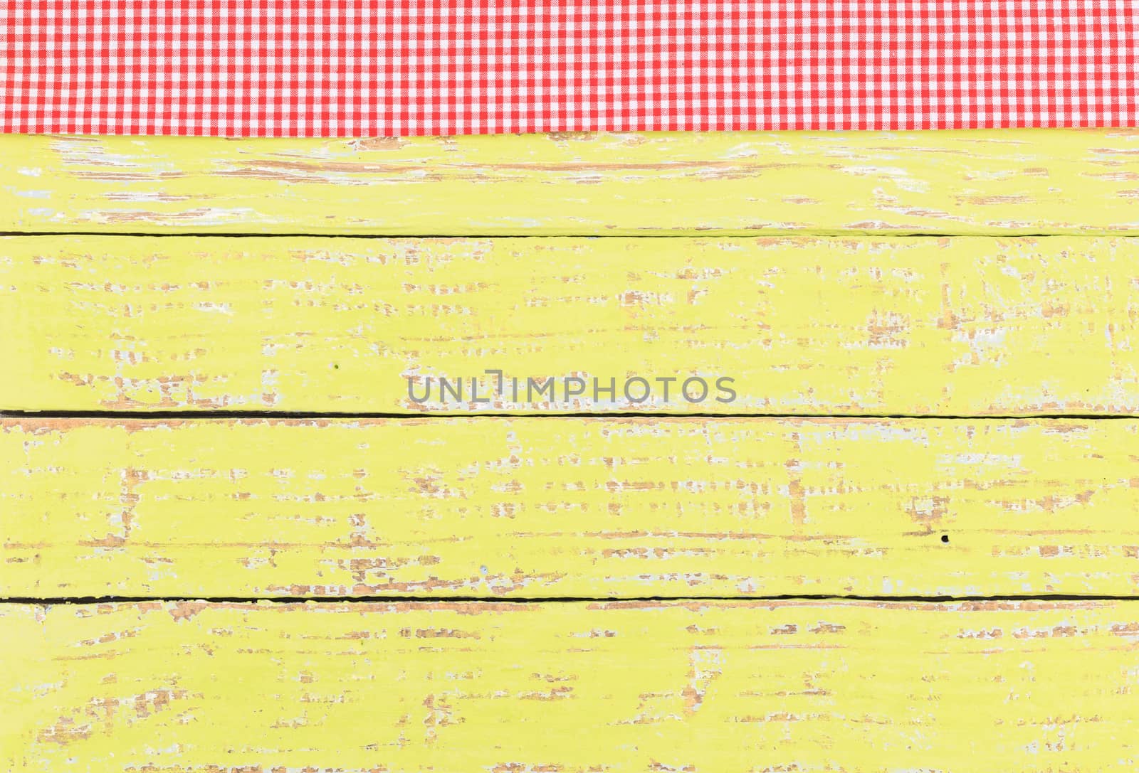 Rustic yellow wooden table surface with red checkered cloth, top view