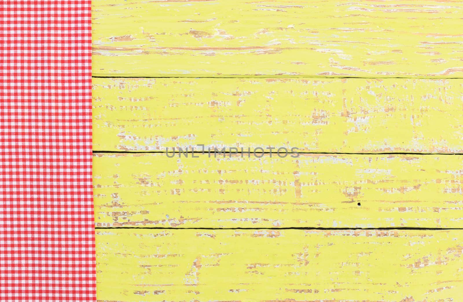 Red checked tablecloth on rustic colored wooden table background, top view
