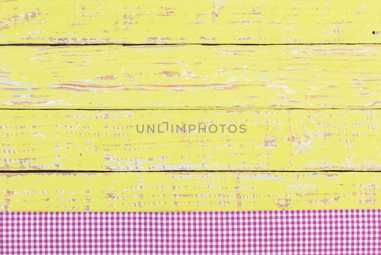 Rustic yellow wooden table surface with purple checkered cloth, top view