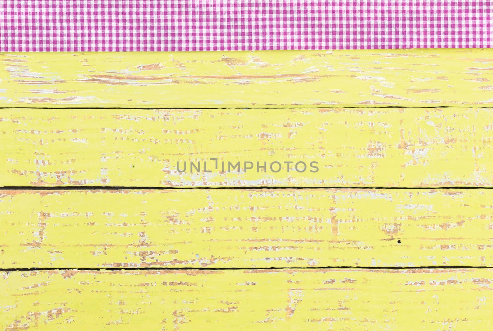 Rustic yellow wooden table surface with purple checkered cloth, top view