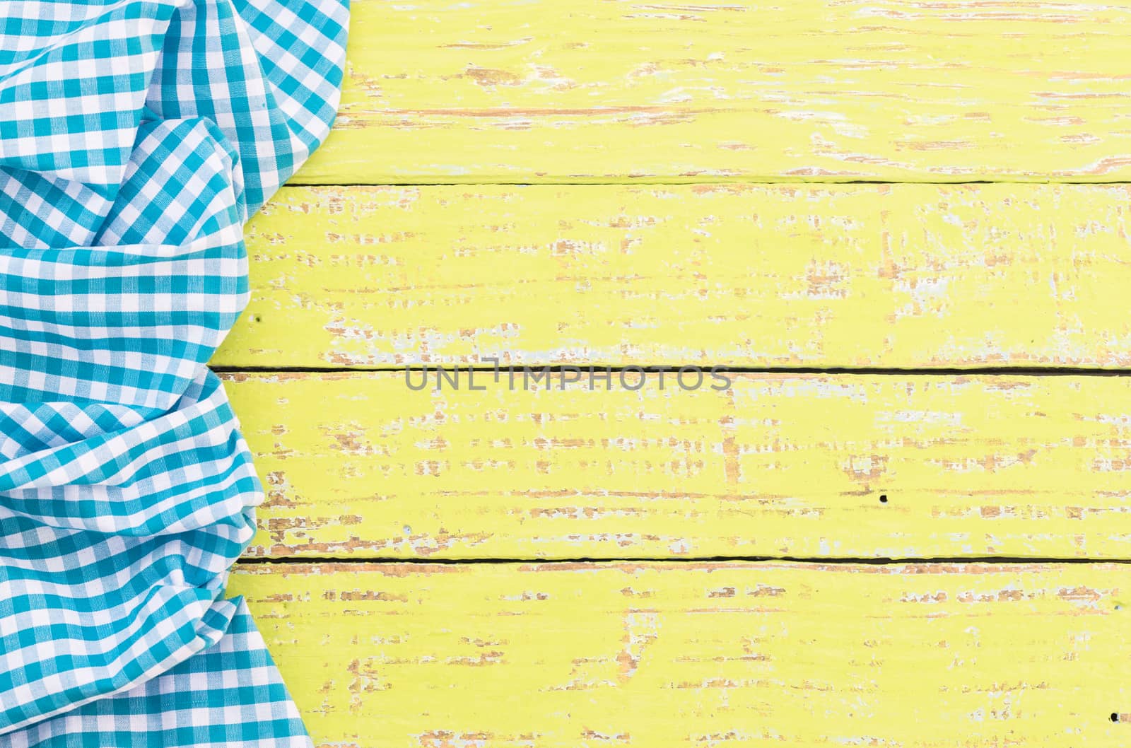 Yellow wooden table surface with rustic blue checkered cloth, top view