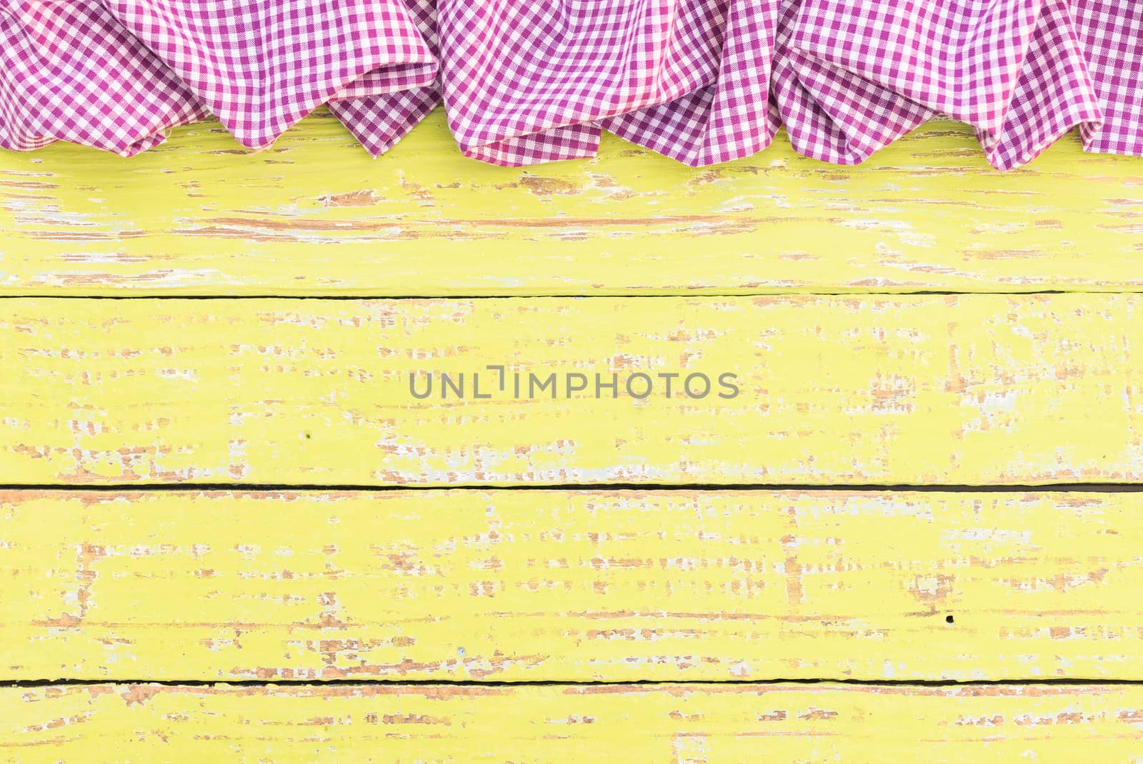 Rustic yellow wooden table surface with purple checkered cloth, top view