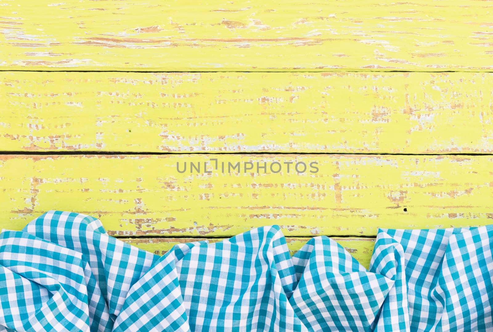 Yellow wooden table surface with rustic blue checkered cloth, top view