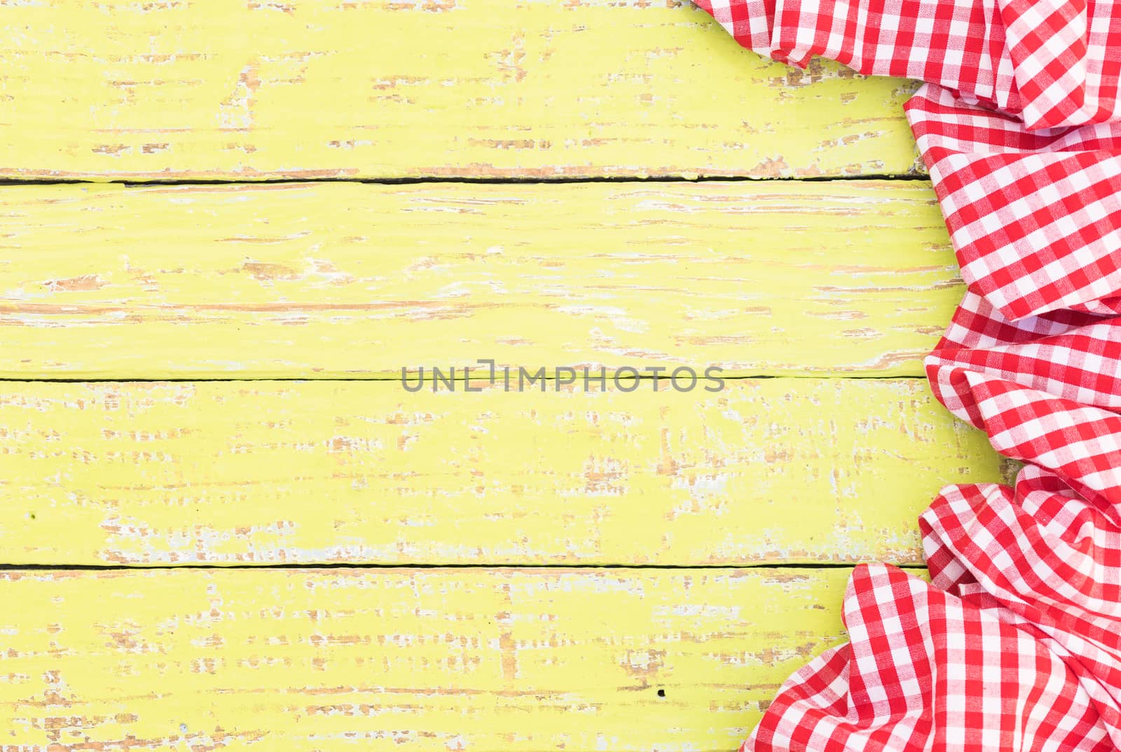 Yellow wooden table surface with rustic red checkered cloth, top view