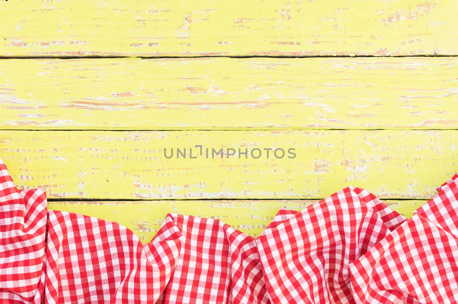 Rustic yellow wooden table surface with red checkered cloth, top view