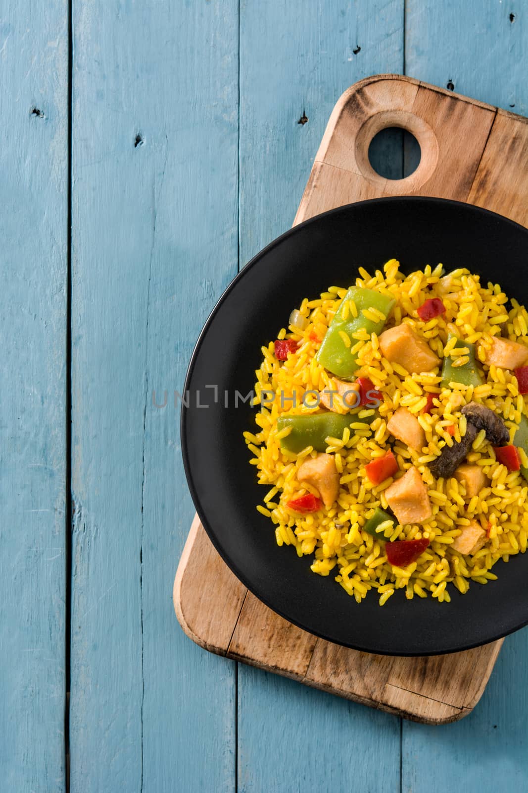 Fried rice with chicken and vegetables on black plate on blue wooden table