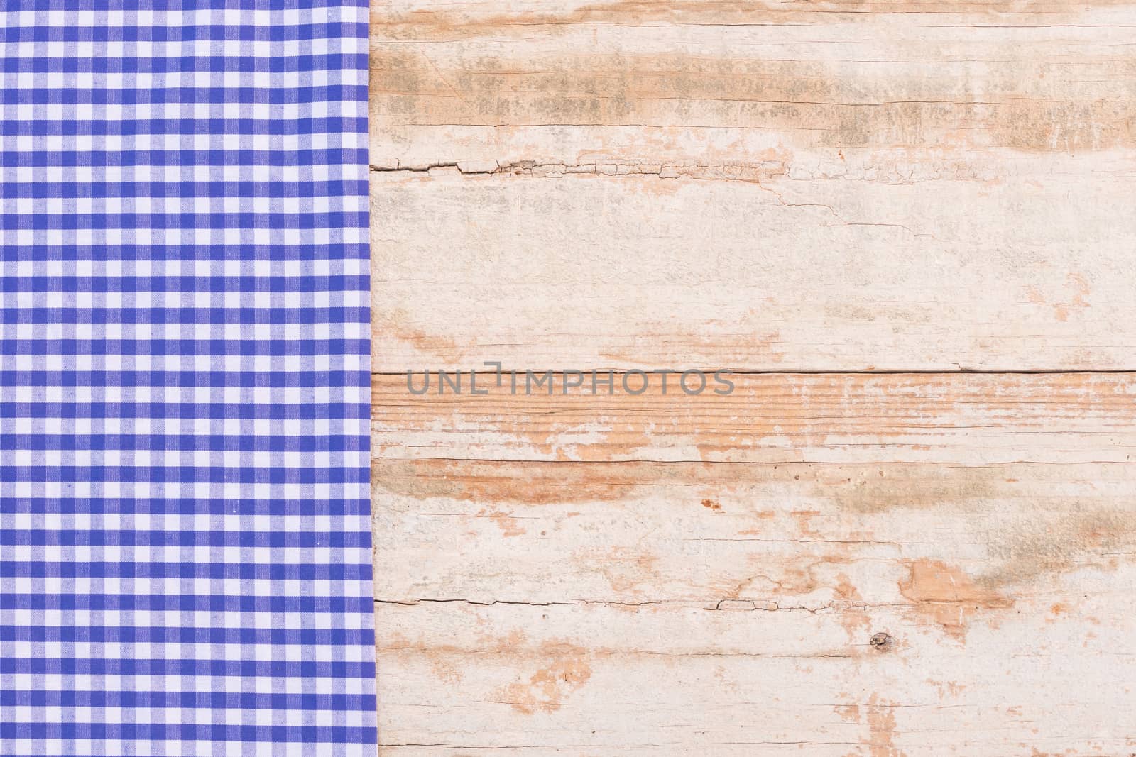 Blue checked tablecloth on rustic wooden table background, top view