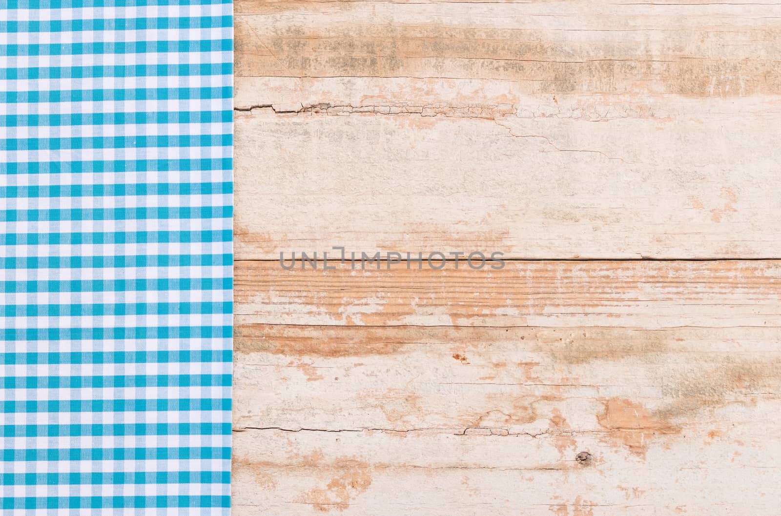 Blue checked tablecloth on rustic wooden table background, top view