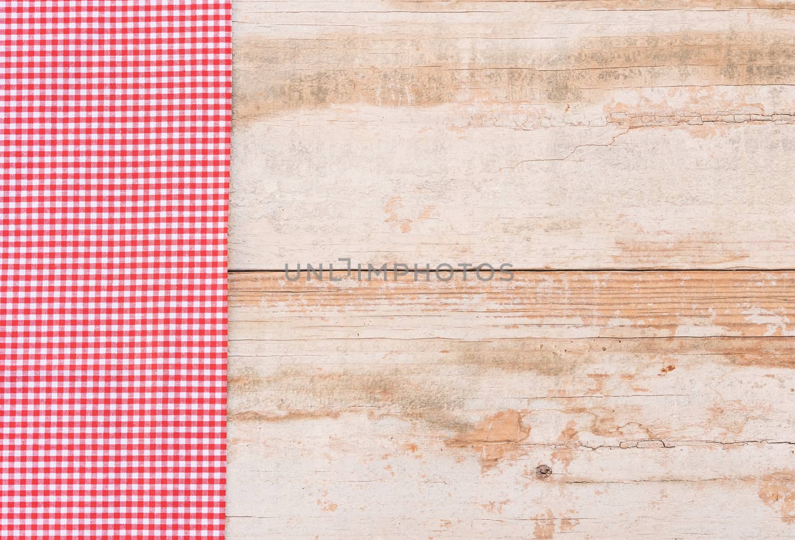 Red checked tablecloth on rustic wooden table background, top view