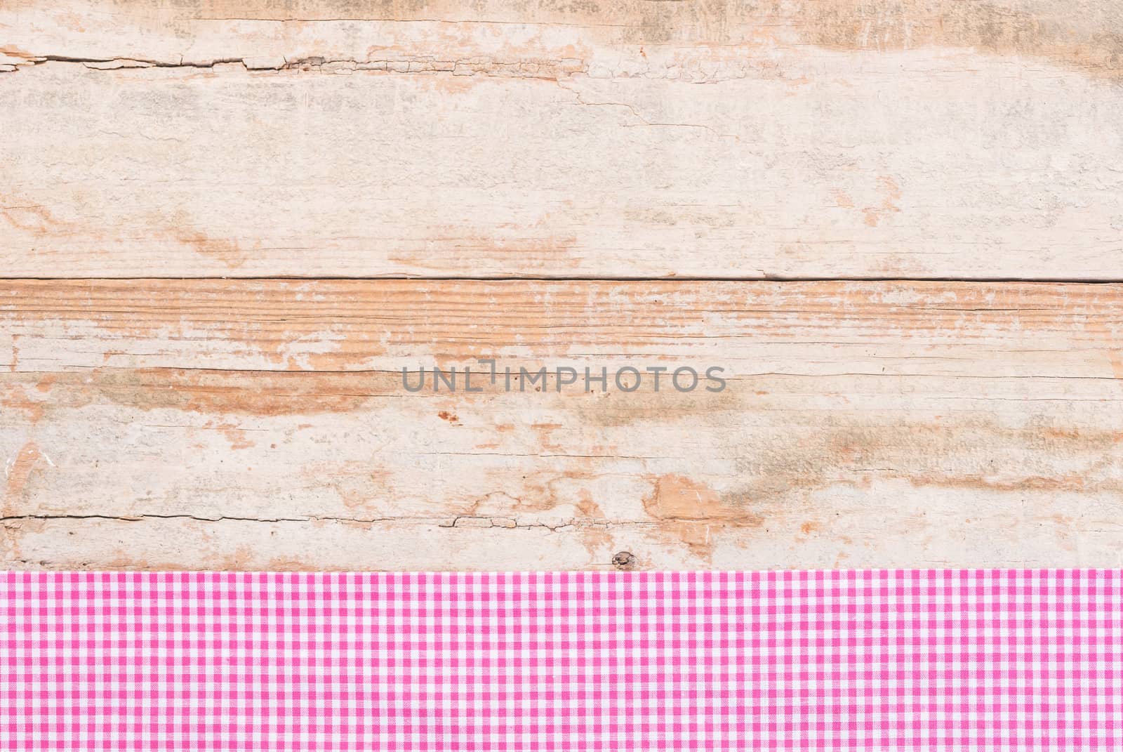 Rustic wooden table surface with pink checkered cloth, top view