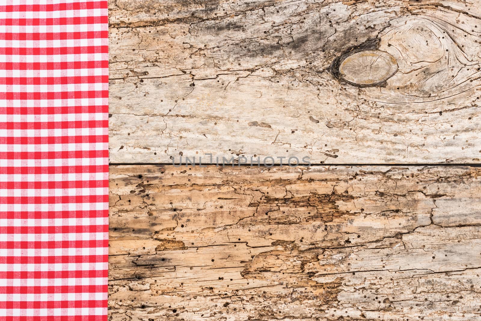 Red checked tablecloth on rustic wooden table background, top view