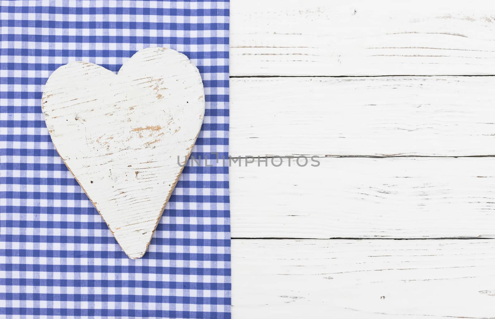 Rustic white heart on blue checked textile and white wooden background with copy space