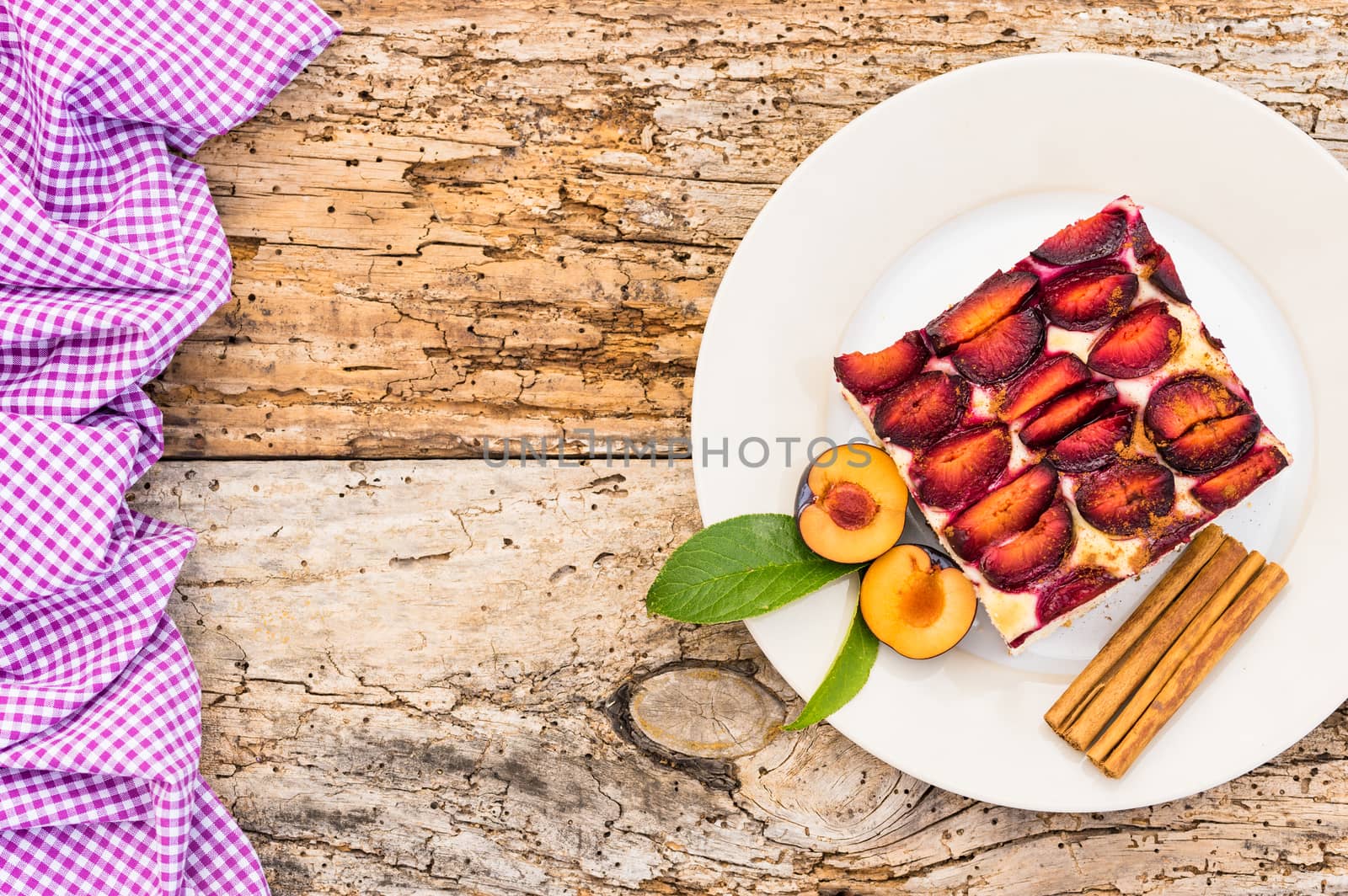 Delicious piece of cake with fresh plums and cinnamon on rustic wooden table