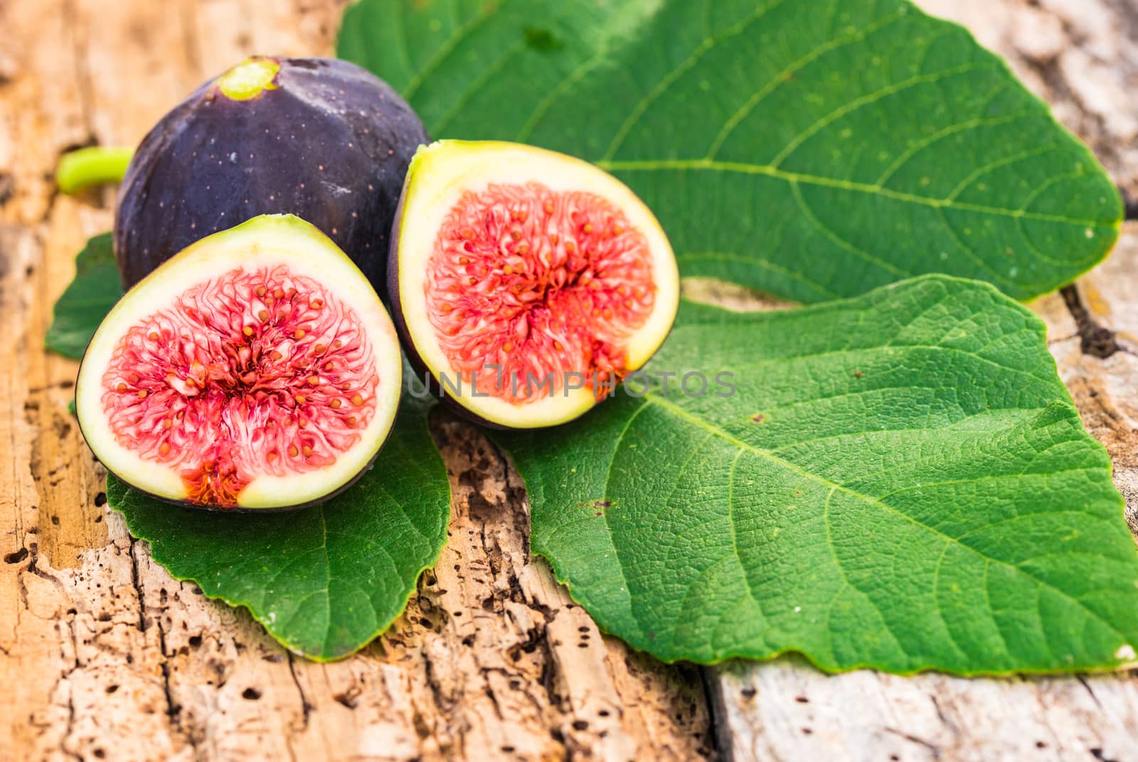 Fresh fig fruits with green leaves, close-up on rustic wooden background