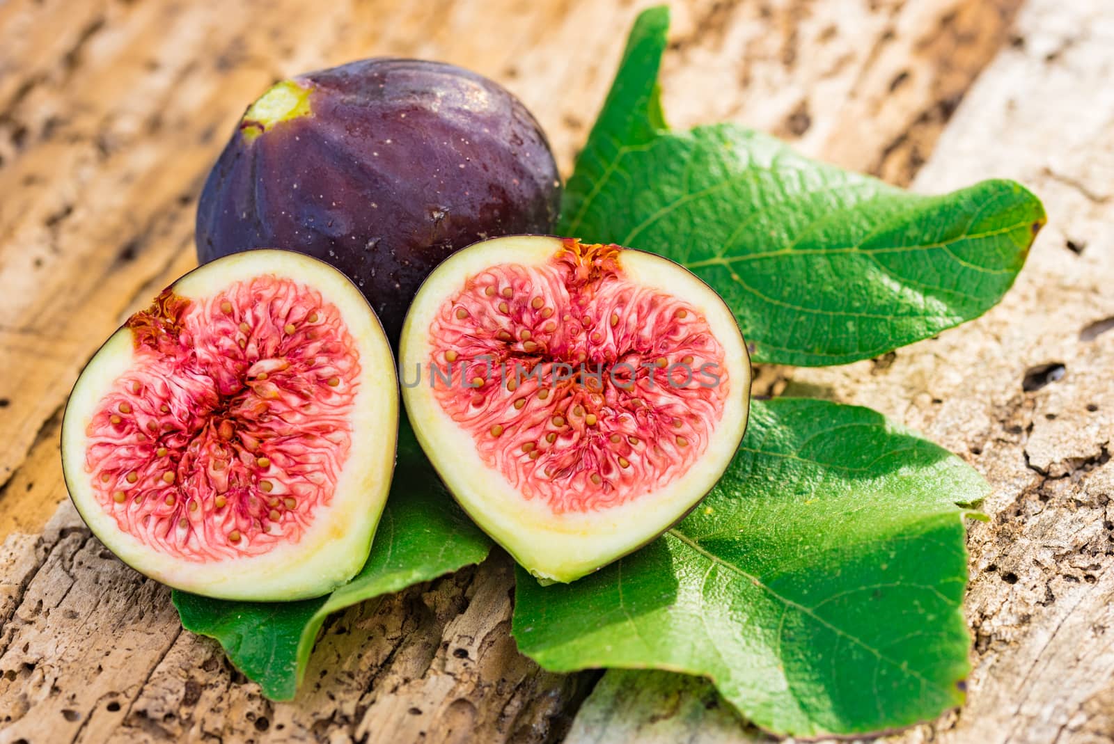 Close-up of fresh figs with green leaves on wooden table background
