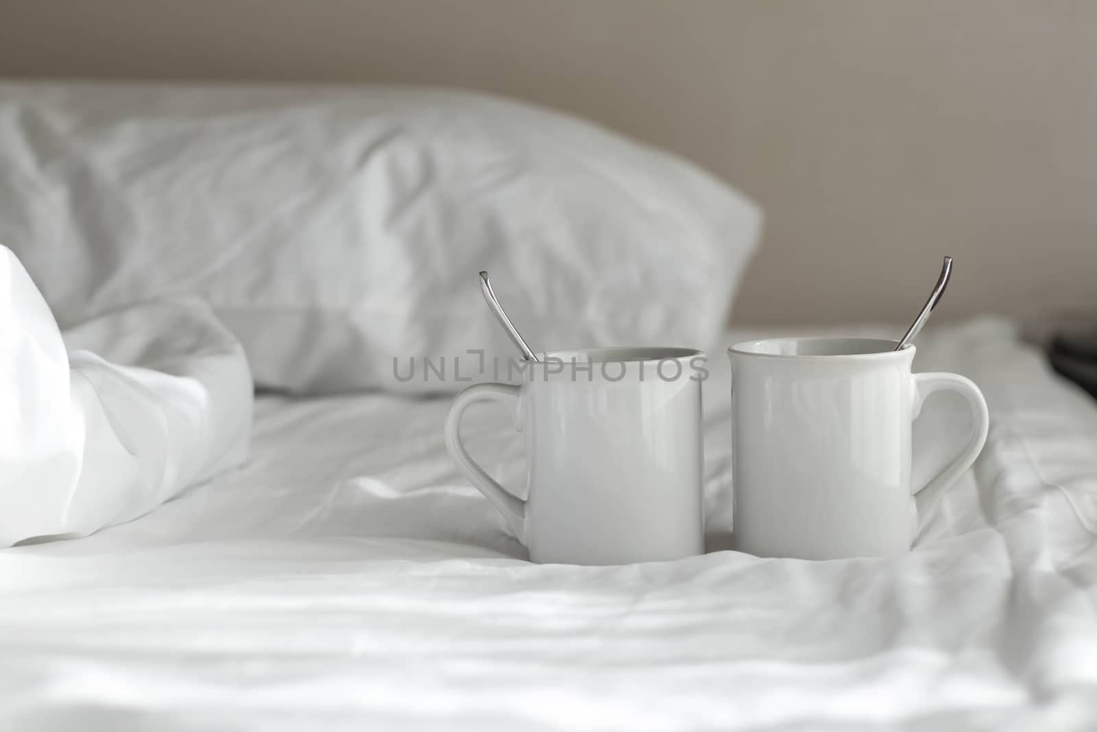 Two white coffee mug with spoon lay on the bed in the morning. by Eungsuwat