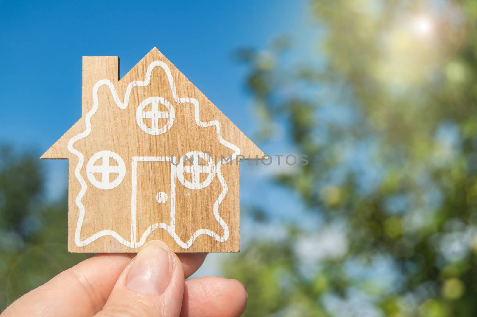 Toy wooden House in hand against the summer sky. The concept of real estate and insurance, the dream of your own home.