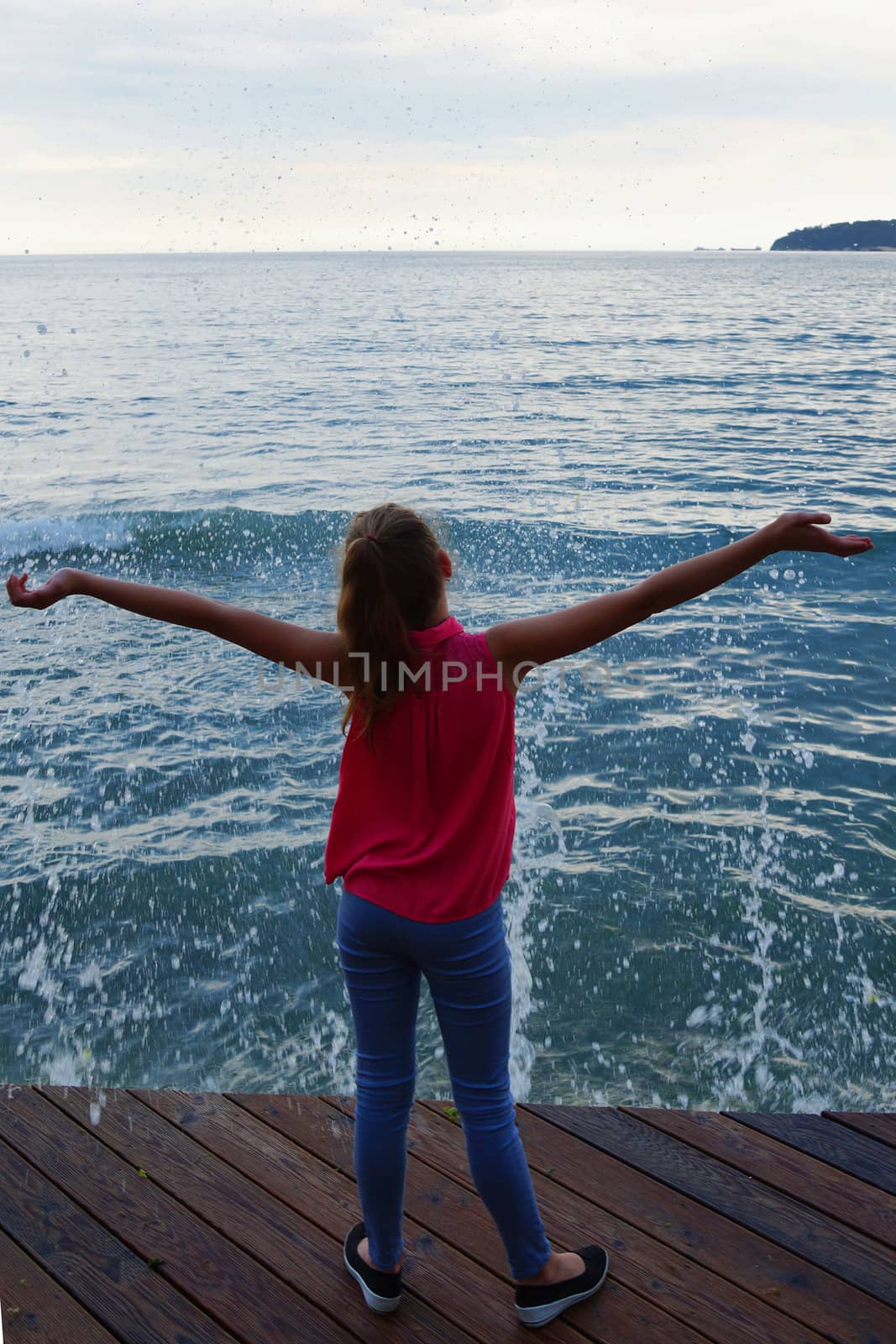 girl on a wooden pier with arms raised looks at the stormy sea