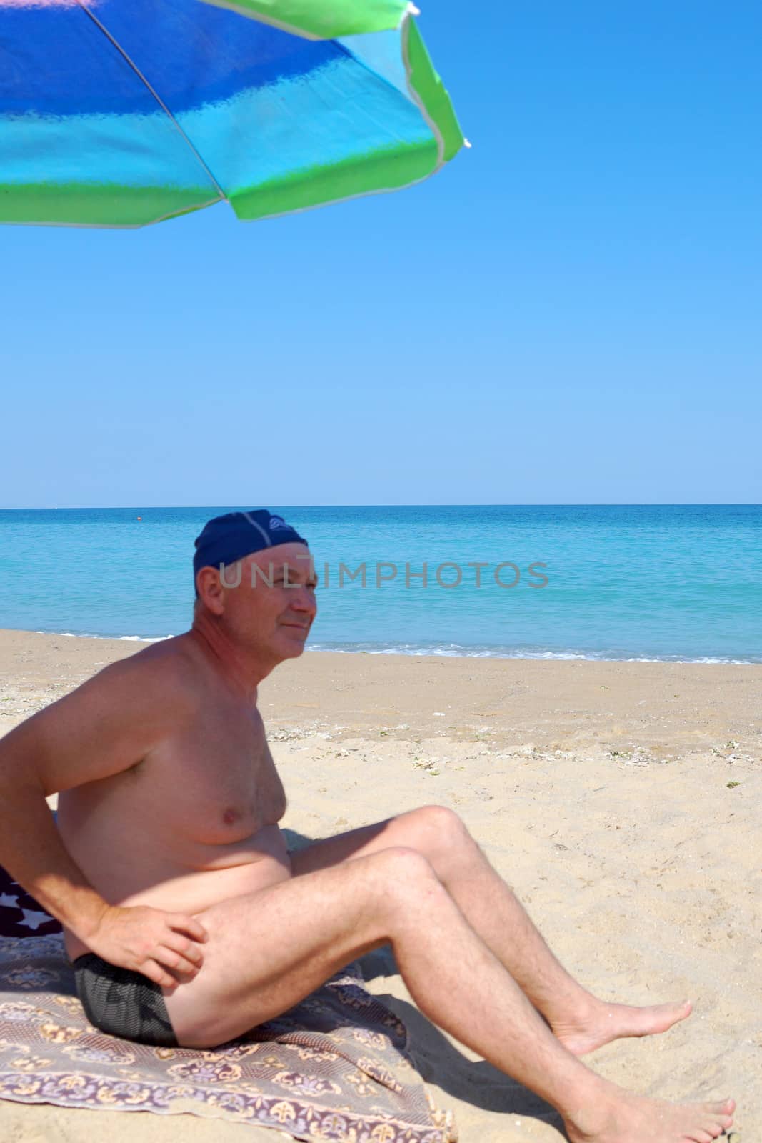 man sitting under a beach umbrella on an empty beach.