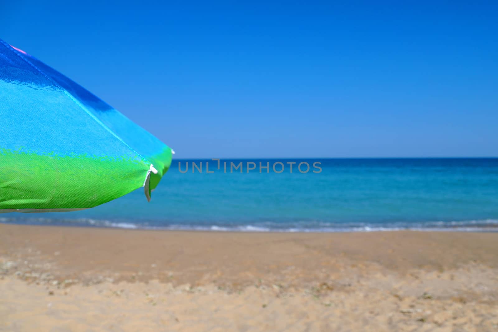 beach umbrella on an empty sandy beach against a clear horizon. by Annado