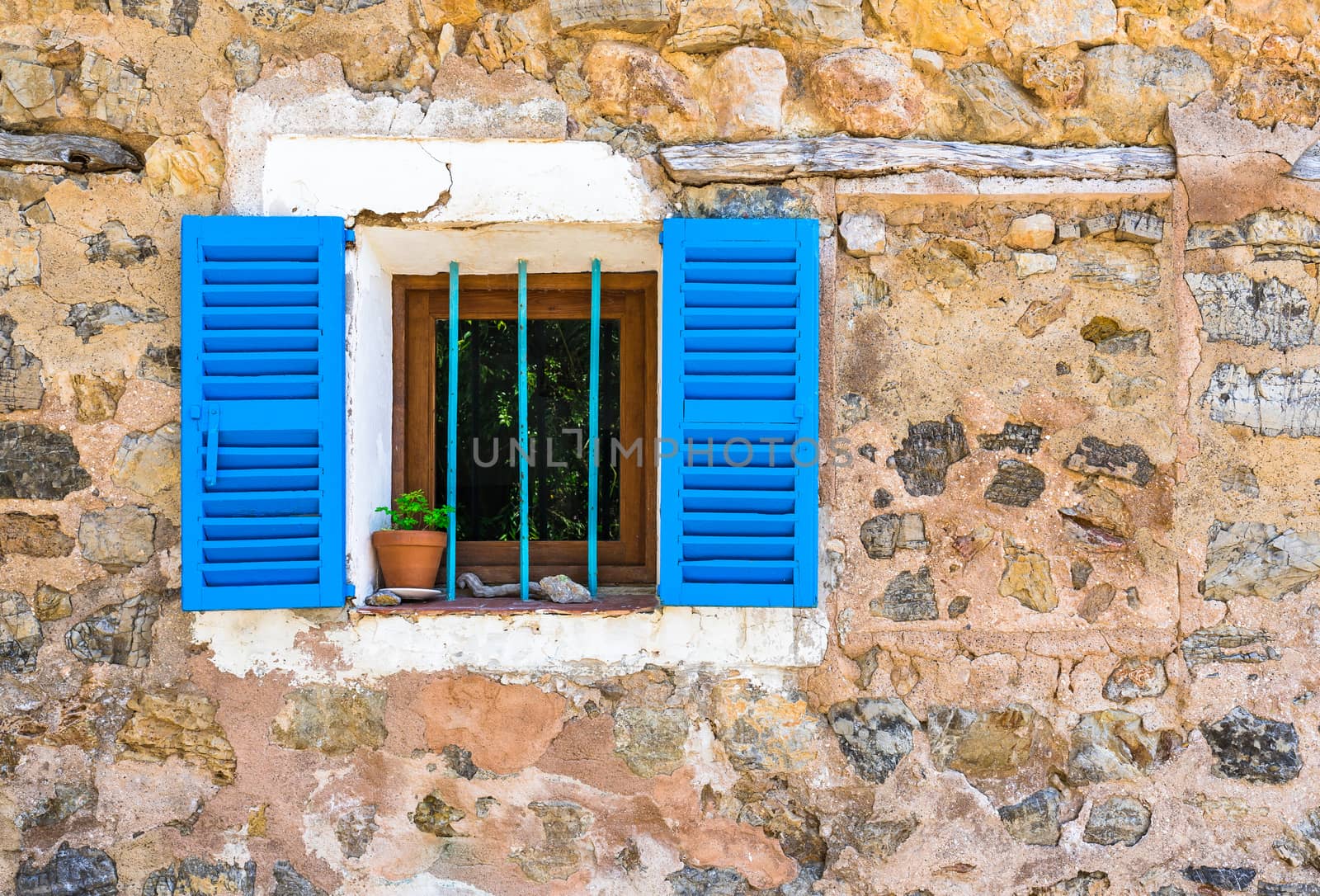 Detail view of stone wall and window with blue shutters of mediterranean house