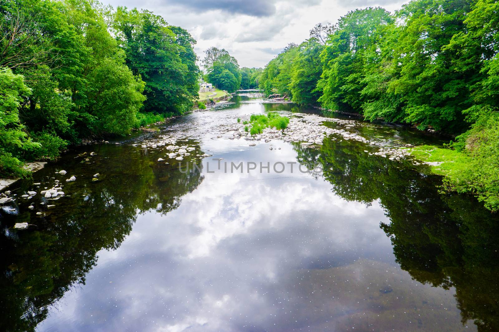 standing on a bridge looking down a slow moving river with green banks