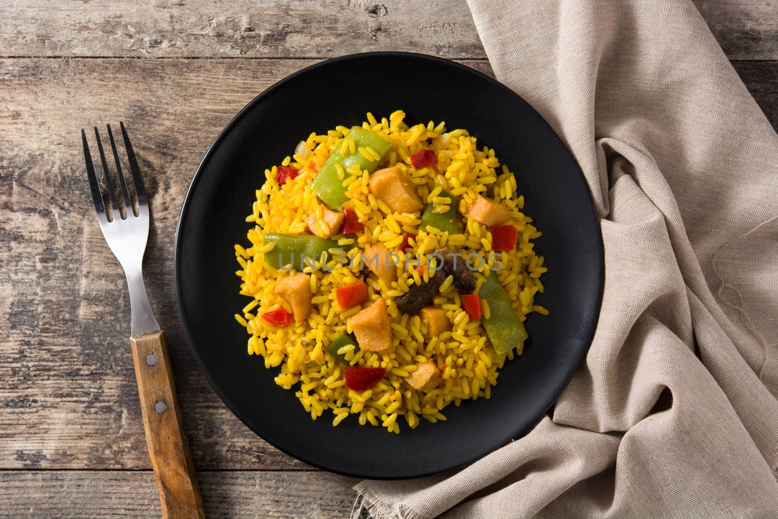 Fried rice with chicken and vegetables on black plate on wooden table