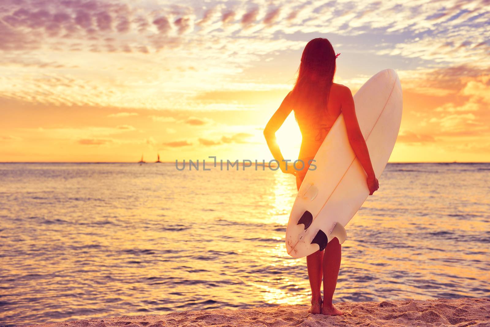 Surfer girl surfing looking at ocean beach sunset. Beautiful sexy female bikini woman looking at water with standing with surfboard having fun living healthy active lifestyle. Water sports with model.