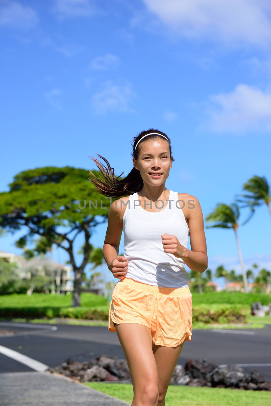 Young woman jogging on city street during summer. Asian girl doing cardio exercise training the body to lose weight and staying fit and in shape. Portrait waist up of female jogger going for a run.