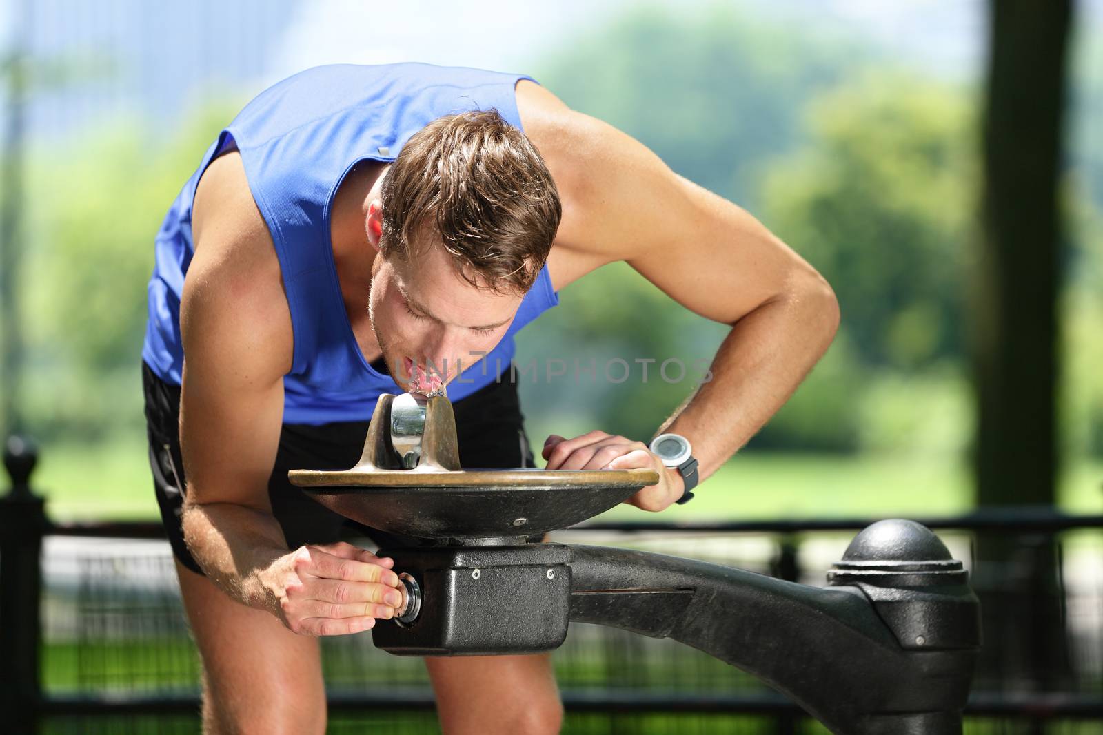 Sport man drinking water from public park fountain by Maridav