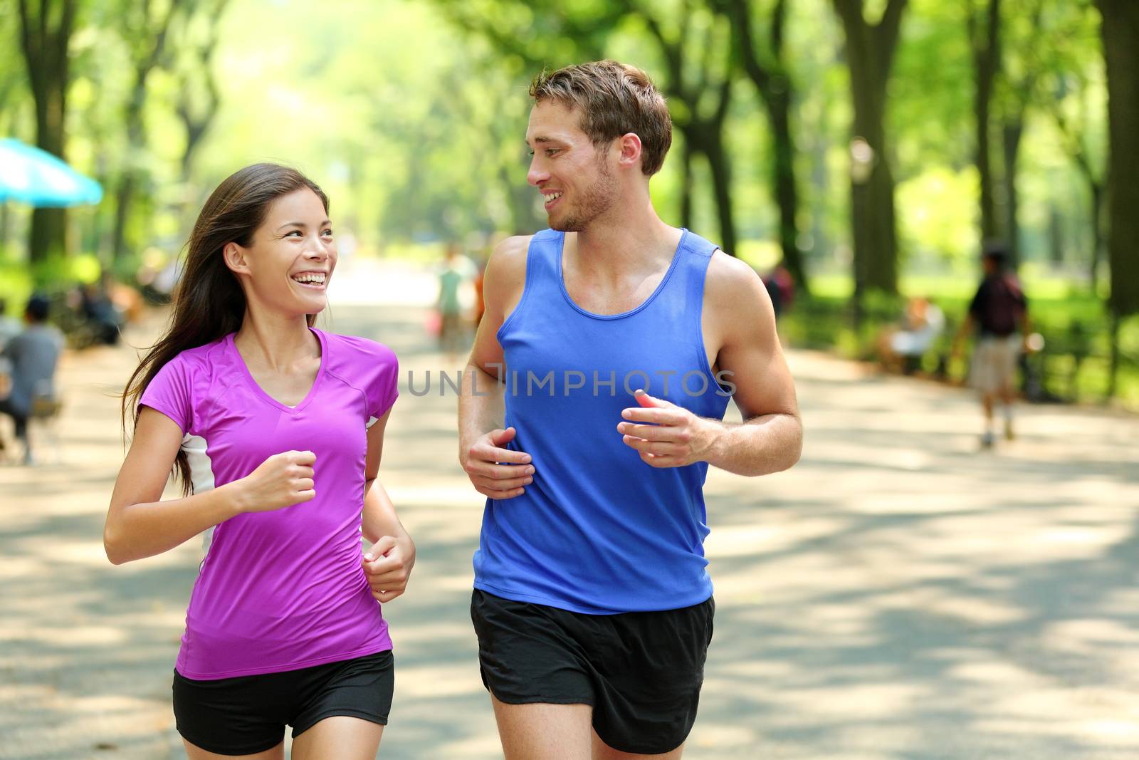 Running couple training in Central Park, New York City (NYC). Happy runners talking together during run on famous Mall walk path under trees in Manhattan, urban fitness.